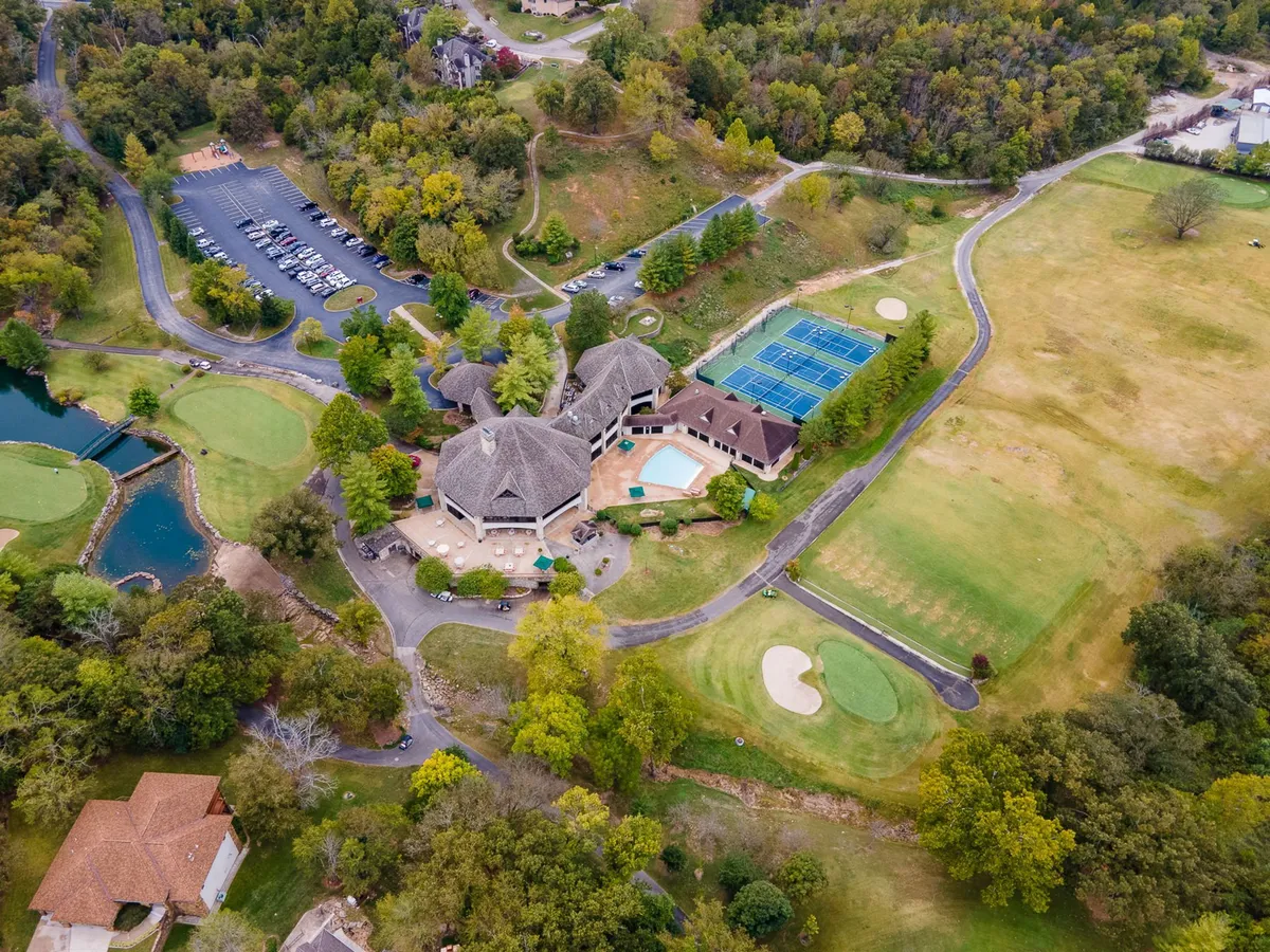 A sweeping view showcases the resort's key amenities: a manicured golf course in the foreground, a sparkling swimming pool with inviting lounge chairs, well-maintained tennis courts, and the clubhouse, all surrounded by lush greenery. The image captures guests enjoying various activities, with sunlight creating a warm, relaxed atmosphere.