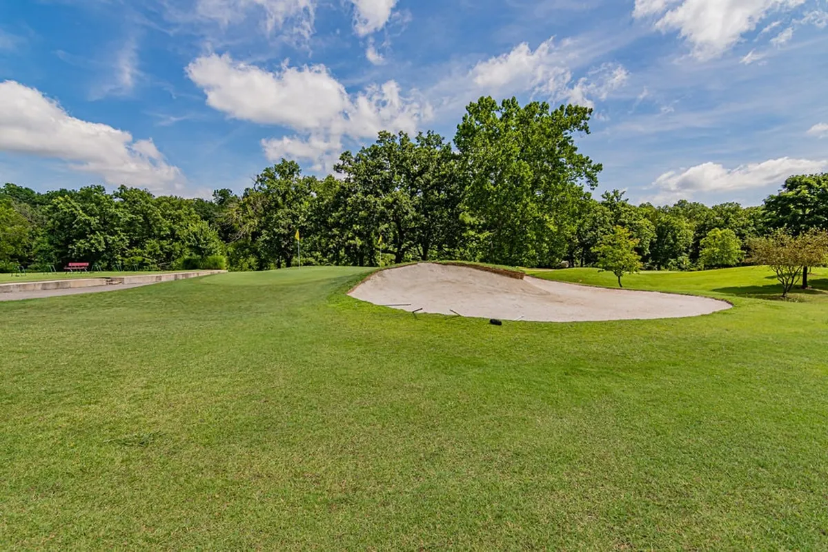 A lush golf course scene featuring a sand trap, rolling green grass, and distant trees. The open, manicured landscape is inviting and hints at exclusive golf access for guests.