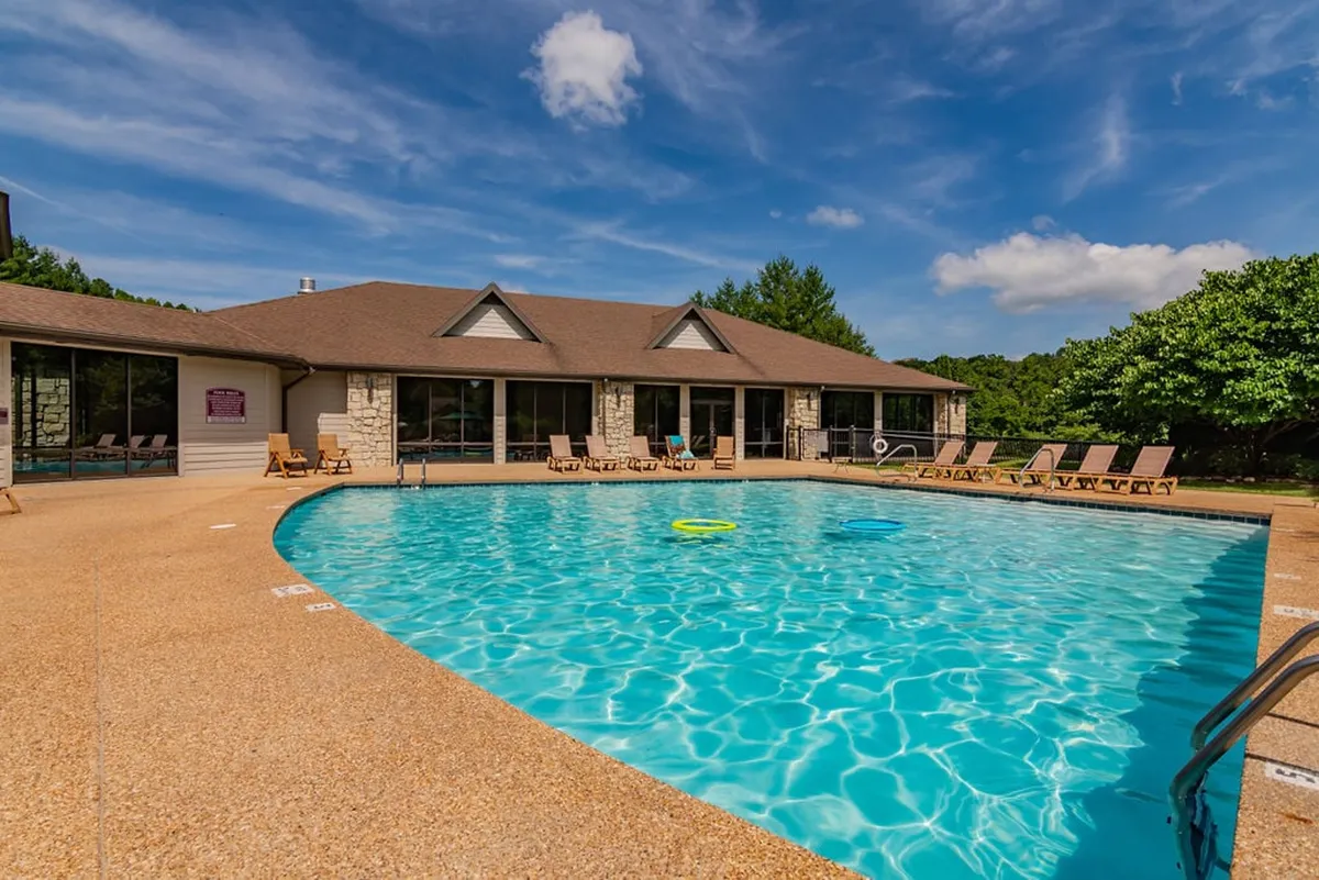 A vibrant exterior scene of a swimming pool area, featuring lounge chairs and the building exterior in the background. The mood is relaxed, with space for swimming, sunbathing, and socializing under open skies.