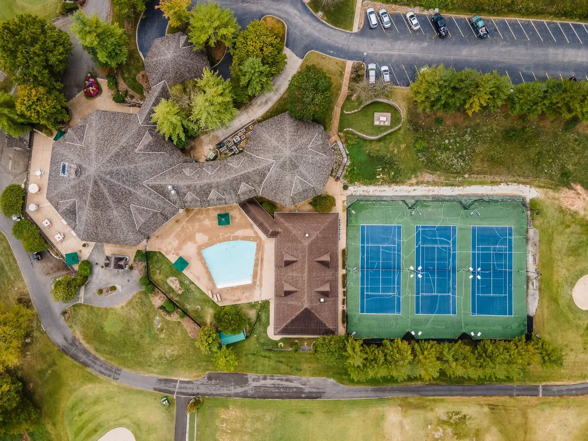 This vibrant exterior shot captures the resort's main swimming pool alongside tennis courts and lush surroundings. The scene is active and welcoming, showing both water and courts, perfectly illustrating the variety of family-friendly amenities available for outdoor fun at Stonebridge Resort.