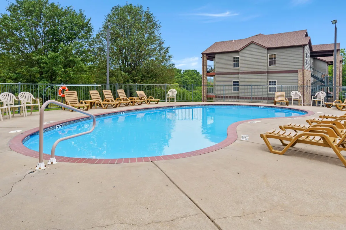 A sparkling swimming pool surrounded by lounge chairs and leafy trees, with a building façade in the background. The pool area conveys relaxation, social opportunities, and leisure amenities available to guests.