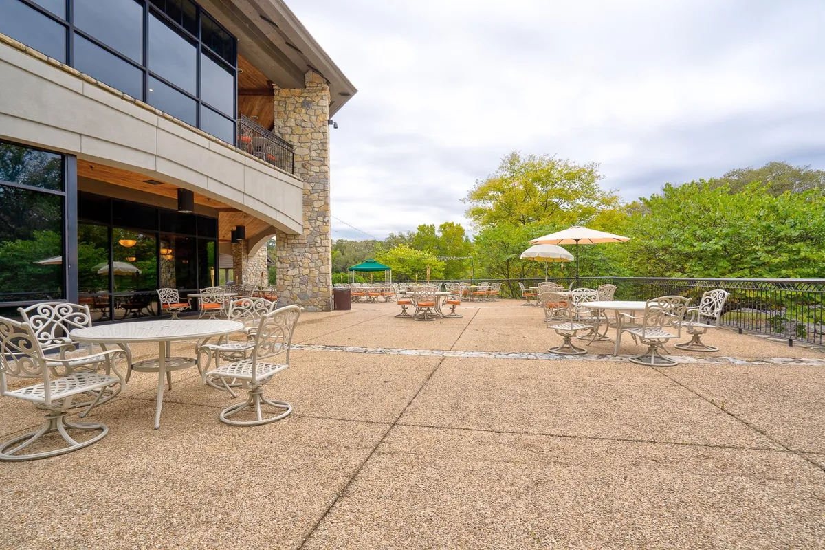 An outdoor seating area set against a stone building, surrounded by greenery. The seating is arranged for dining or social gatherings, with natural sunlight illuminating the space, inviting both social and solitary moments overlooking resort grounds.
