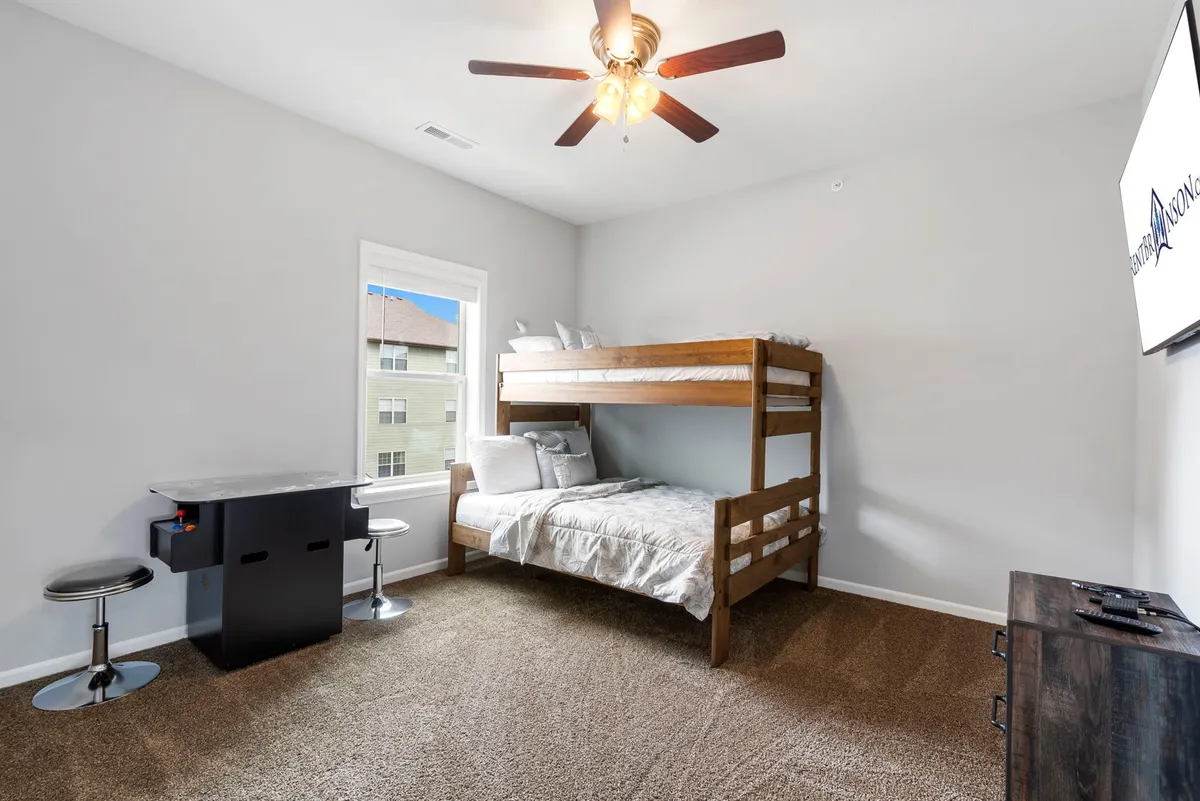 A cheerful bunk bedroom, complete with a sturdy bunk bed, window for natural light, a small dining table with stools, and a television. The room is playful yet comfortable, ideal for kids or singles, and exudes a sense of fun and coziness.