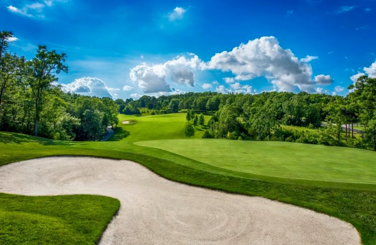 A striking view over the golf course features a carefully maintained sand trap, rolling green fairway, and a brilliant blue sky dotted with clouds. The landscape suggests both championship-level play and tranquil moments, with open space and lush landscaping inviting both golfers and those seeking scenic relaxation.