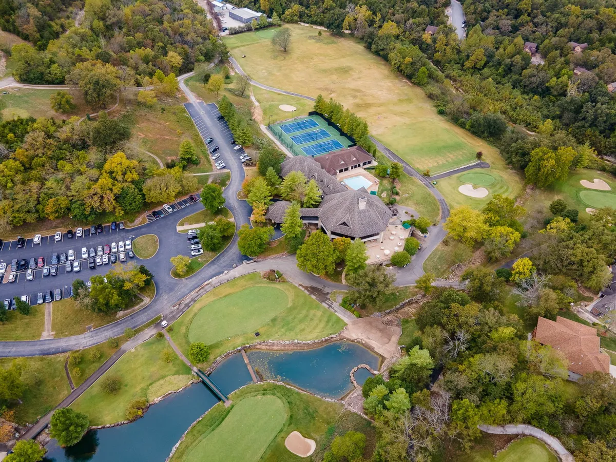 A broad exterior view captures not just the golf course but also tennis courts, a clubhouse, parking area, and tranquil ponds. The scene is lively yet laid-back, showing a variety of outdoor amenities and the community hub aspect of the resort environment.
