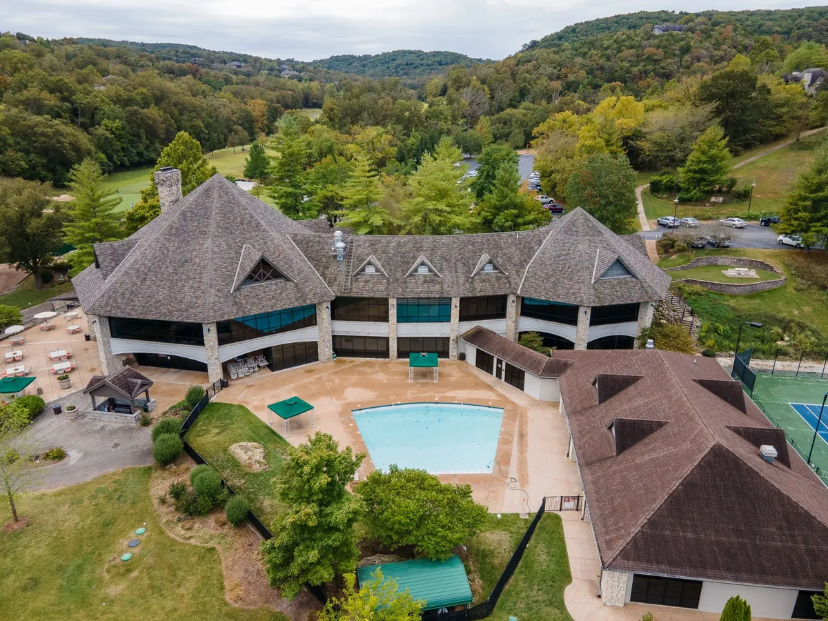 A beautiful exterior scene highlights the resort's pool, complete with lounge chairs, adjacent tennis courts, lush landscaping, and the impressive architecture of the main building. The relaxed mood is enhanced by the elegant surroundings and ample space for guests to unwind or socialize.