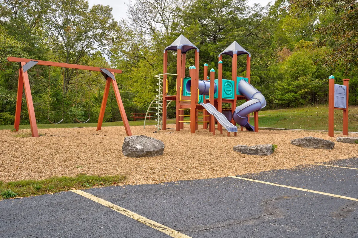 A cheerful exterior view of a playground, complete with swings, climbing frames, and surrounding greenery. Children are seen actively playing, which conveys the resort's appeal to families with young kids looking for safe, engaging spaces.