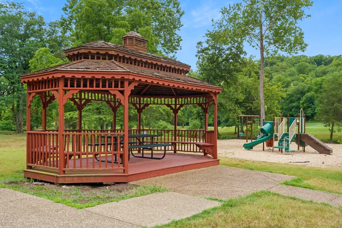 A joyful scene at the playground, with a gazebo for shaded gatherings and modern play equipment set amid trees and open space. Children play while families relax nearby, capturing the spirit of fun and community.